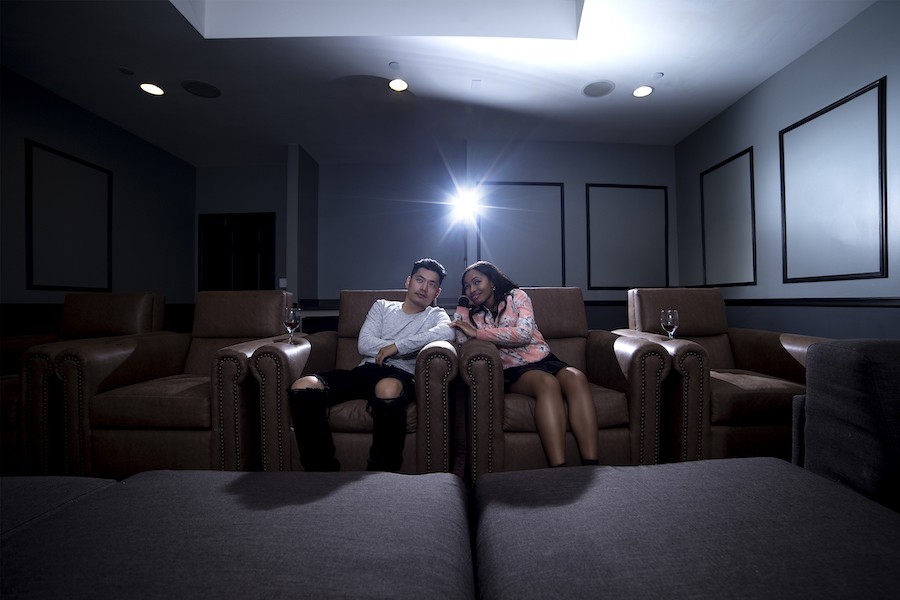 A casual home theater with a man and woman sitting in comfortable chairs with cupholders.